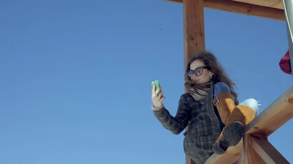 Mulher usando Smartphone Relaxa no banco em Beautiful Park. Jovem mulher em fazer gestos na tela do telefone. Tecnologia ao ar livre — Fotografia de Stock