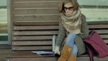 Genç kadın bir bahar parkta bir bankta oturan bir termos şişe çay içme