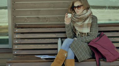 Genç kadın bir bahar parkta bir bankta oturan bir termos şişe çay içme