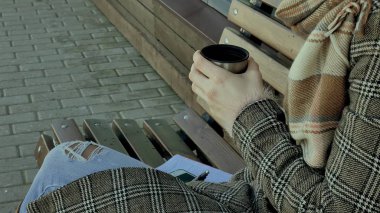 Genç kadın bir bahar parkta bir bankta oturan bir termos şişe çay içme