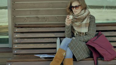 Genç kadın bir bahar parkta bir bankta oturan bir termos şişe çay içme