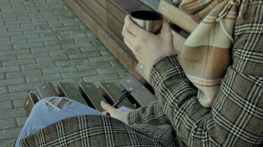 Genç kadın bir bahar parkta bir bankta oturan bir termos şişe çay içme