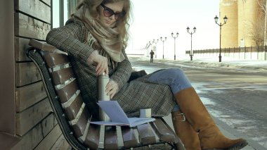 Genç kadın bir bahar parkta bir bankta oturan bir termos şişe çay içme