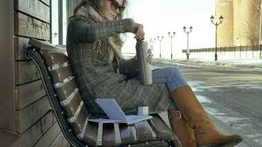 Genç kadın bir bahar parkta bir bankta oturan bir termos şişe çay içme