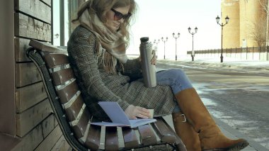 Genç kadın bir bahar parkta bir bankta oturan bir termos şişe çay içme