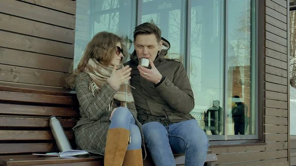 Jeune femme et homme buvant du thé dans une bouteille thermos dans un parc de printemps assis sur un banc — Photo
