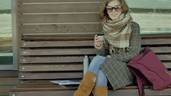 Genç kadın bir bahar parkta bir bankta oturan bir termos şişe çay içme — Stok fotoğraf