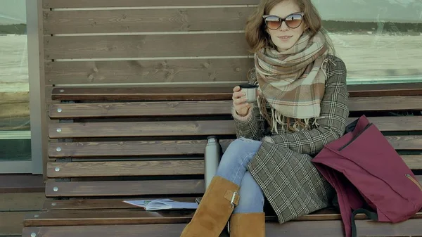 Mujer joven bebiendo té de una botella de termo en un parque de primavera sentado en un banco — Foto de Stock