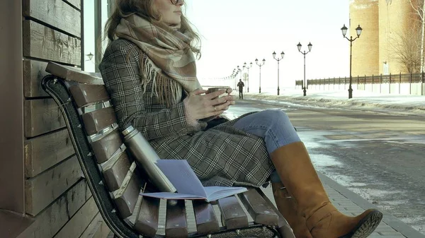 Ung kvinna dricka te från en termos i en spring park sitter på en bänk — Stockfoto