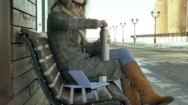 Young woman drinking tea from a thermos bottle in a spring park sitting on a bench — Stock Photo, Image