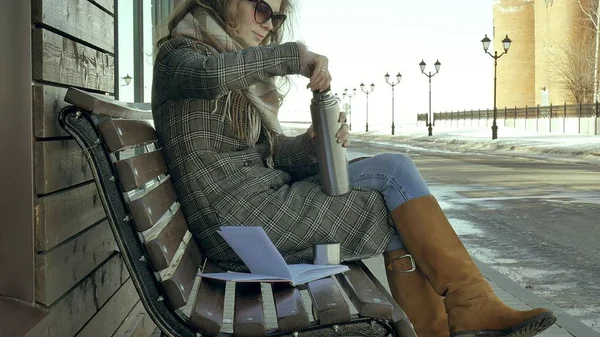 Genç kadın bir bahar parkta bir bankta oturan bir termos şişe çay içme