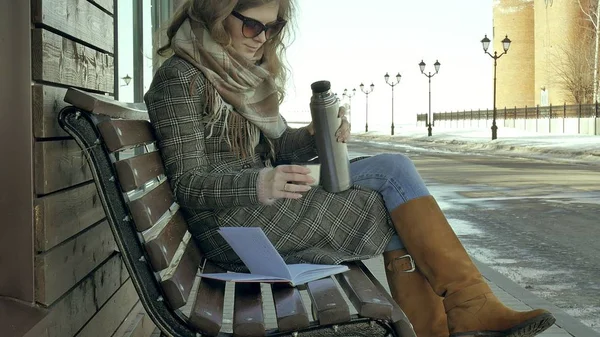Genç kadın bir bahar parkta bir bankta oturan bir termos şişe çay içme