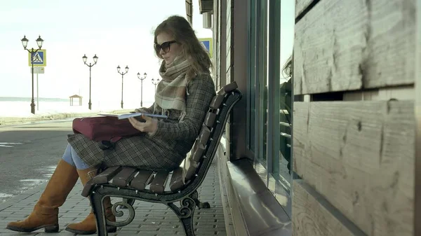 Молода, красива, мила жінка сидить на лавці в парку, в руках свого записника. Вона носить пальто. Вона робить нотатки і виглядає дуже романтично . — стокове фото