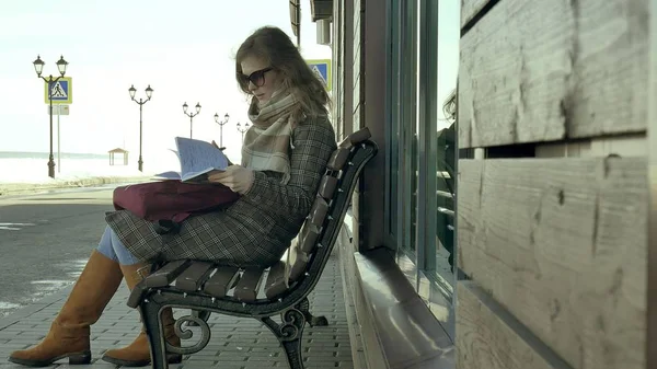 Ung, vacker, härlig kvinna som sitter på bänken i parken, i händerna på hennes anteckningsbok. Hon är klädd i en kappa. Hon gör anteckningar och ser mycket romantisk. — Stockfoto