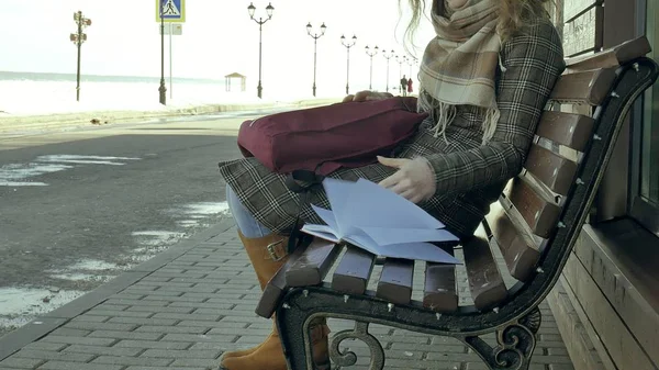 Gyönyörű, szép és fiatal nő ül a padon a parkban, kezében a notebook. Ő visel kabátot. Ő teszi a jegyzeteket, és úgy néz ki, nagyon romantikus. — Stock Fotó