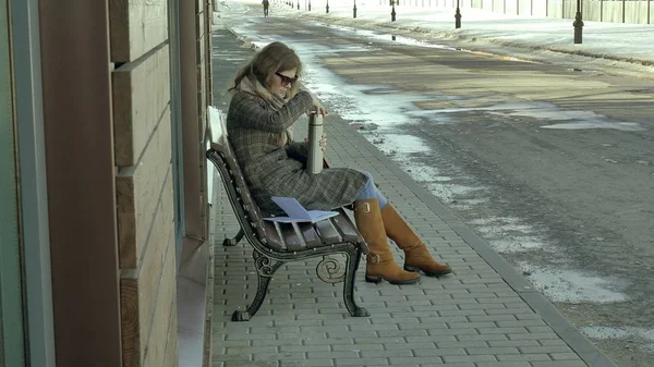 벤치에 앉아 봄 공원에서 보온병 병에서 차를 마시는 젊은 여자 — 스톡 사진