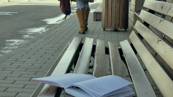 Jonge, prachtige, mooie vrouw zitten op bankje in park, in handen van haar notitieblok. Ze is het dragen van een jas. Zij maakt van notities en ziet er zeer romantisch. — Stockfoto