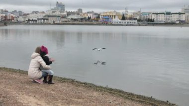 Mutlu ve güzel anne ve kızı nehir kıyısında plaj üzerinde martı besleniyor