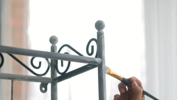 A woman paints black metal furniture with a brush in white — Stock Video