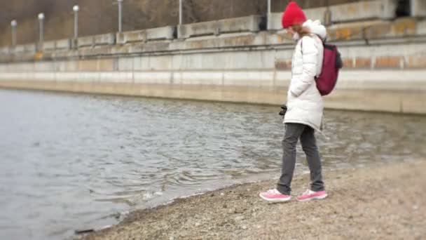 Une belle femme vêtue d'une veste et d'un chapeau rouge se tient debout sur le quai et regarde à travers binoculaire — Video