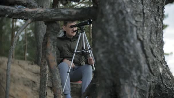 Le vieil homme regarde à travers un télescope dans une forêt sur la rive de la rivière — Video