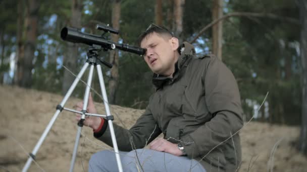 Старик смотрит в телескоп в лесу на берегу реки — стоковое видео