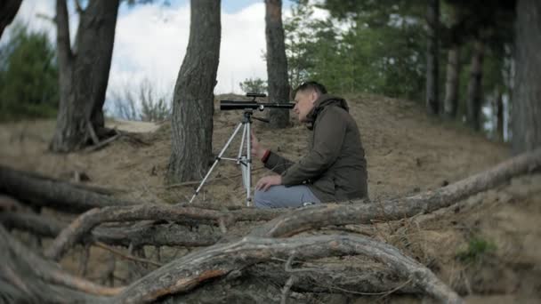 Viejo mira a través de un telescopio en un bosque en la orilla del río — Vídeos de Stock