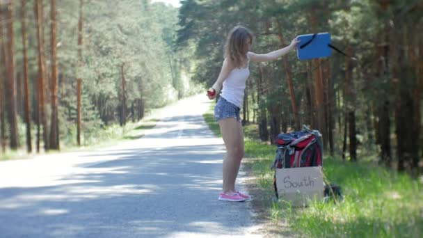 碑文を持つテーブルでバックパックを道路上に若い美しい女性ヒッチハイク立って南 — ストック動画