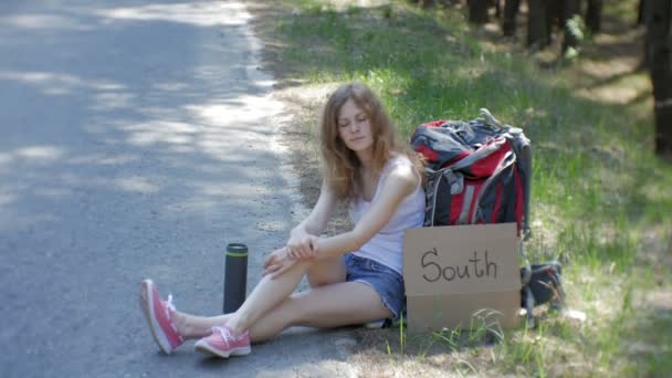 Joven hermosa mujer autostop de pie en la carretera con una mochila en una mesa con una inscripción SUR — Vídeos de Stock