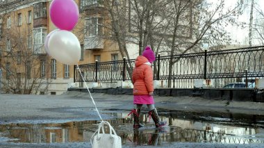 Küçük güzel kız su birikintileri üzerinde renkli balonlar ile yağmur sonra atlama
