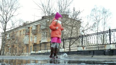 Küçük güzel kız su birikintileri üzerinde yağmur sonrası atlama