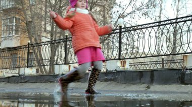 Küçük güzel kız su birikintileri üzerinde yağmur sonrası atlama
