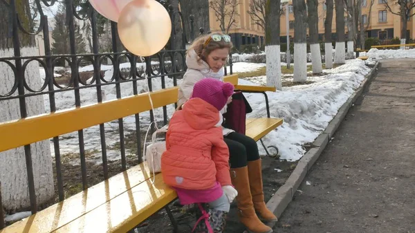 Güzel bir kız ve annesi bir bankta oturan ve lezzetli bir tatlı yeme ve içme çay bir termos erken ilkbaharda — Stok fotoğraf