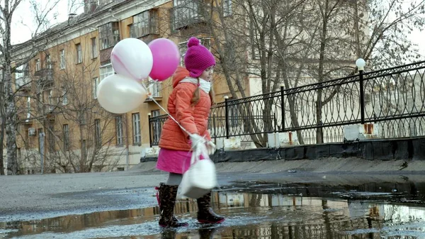 Маленькая красивая девочка прыгает на лужах после дождя с красочными воздушными шарами — стоковое фото