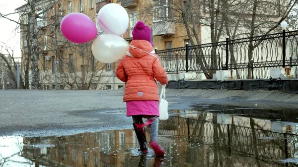 Lilla vackra flicka hoppa på vattenpölar efter regn med färgglada ballonger — Stockfoto