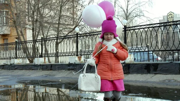 Piccola bella ragazza che salta sulle pozzanghere dopo la pioggia con palloncini colorati — Foto Stock