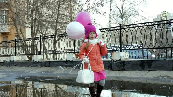 Kleines hübsches Mädchen springt nach Regen mit bunten Luftballons auf Pfützen — Stockfoto