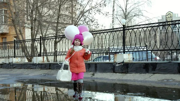 Kleines hübsches Mädchen springt nach Regen mit bunten Luftballons auf Pfützen — Stockfoto