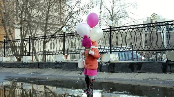 Petite belle fille sautant sur les flaques après la pluie avec des ballons colorés — Photo