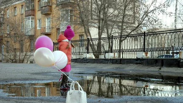 Kleines hübsches Mädchen springt nach Regen mit bunten Luftballons auf Pfützen — Stockfoto