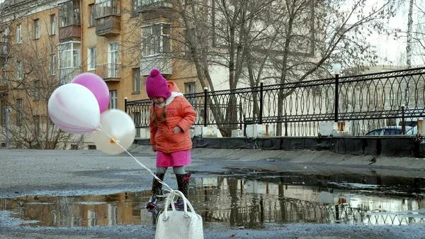 Kleines hübsches Mädchen springt nach Regen mit bunten Luftballons auf Pfützen — Stockfoto