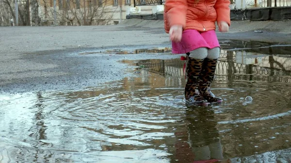 Küçük güzel kız su birikintileri üzerinde yağmur sonrası atlama — Stok fotoğraf