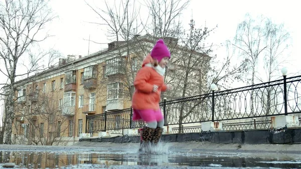 Pequena menina bonita pulando em poças após a chuva — Fotografia de Stock