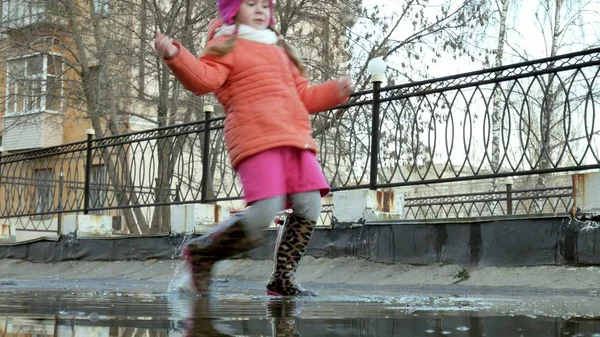 Malá krásná dívka skákání v kalužích po dešti — Stock fotografie