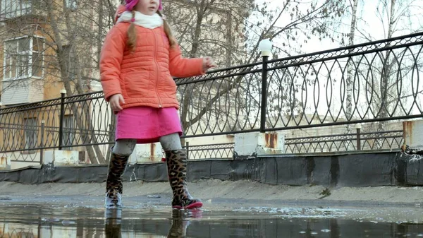 Küçük güzel kız su birikintileri üzerinde yağmur sonrası atlama — Stok fotoğraf