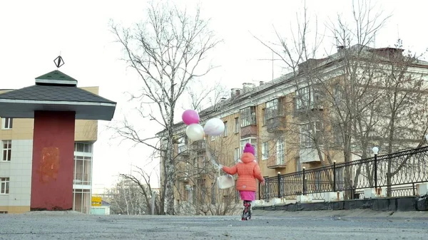 Petite belle fille sautant sur les flaques après la pluie avec des ballons colorés — Photo