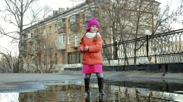 Küçük güzel kız su birikintileri üzerinde yağmur sonrası atlama — Stok fotoğraf