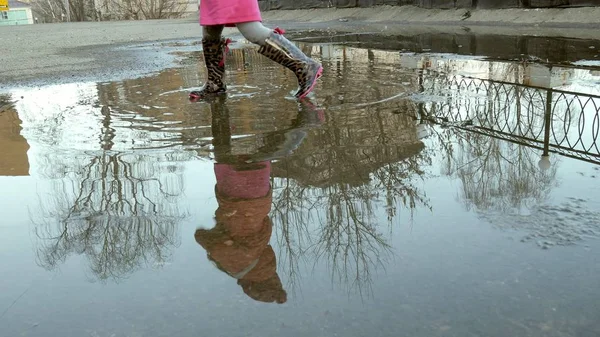 Küçük güzel kız su birikintileri üzerinde yağmur sonrası atlama — Stok fotoğraf