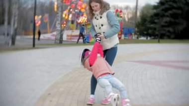 Anne ve kızı tekerlekli paten üzerinde binmek. Kız paten ve falls öğrenme. Anne kızı Silindirler binmek için öğretir