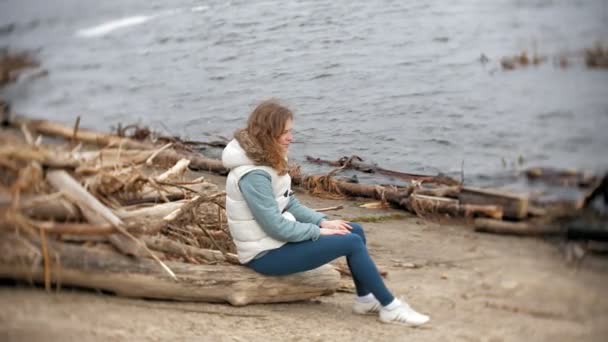 Belle jeune femme marchant le long de la rive et ramassant des branches sèches — Video